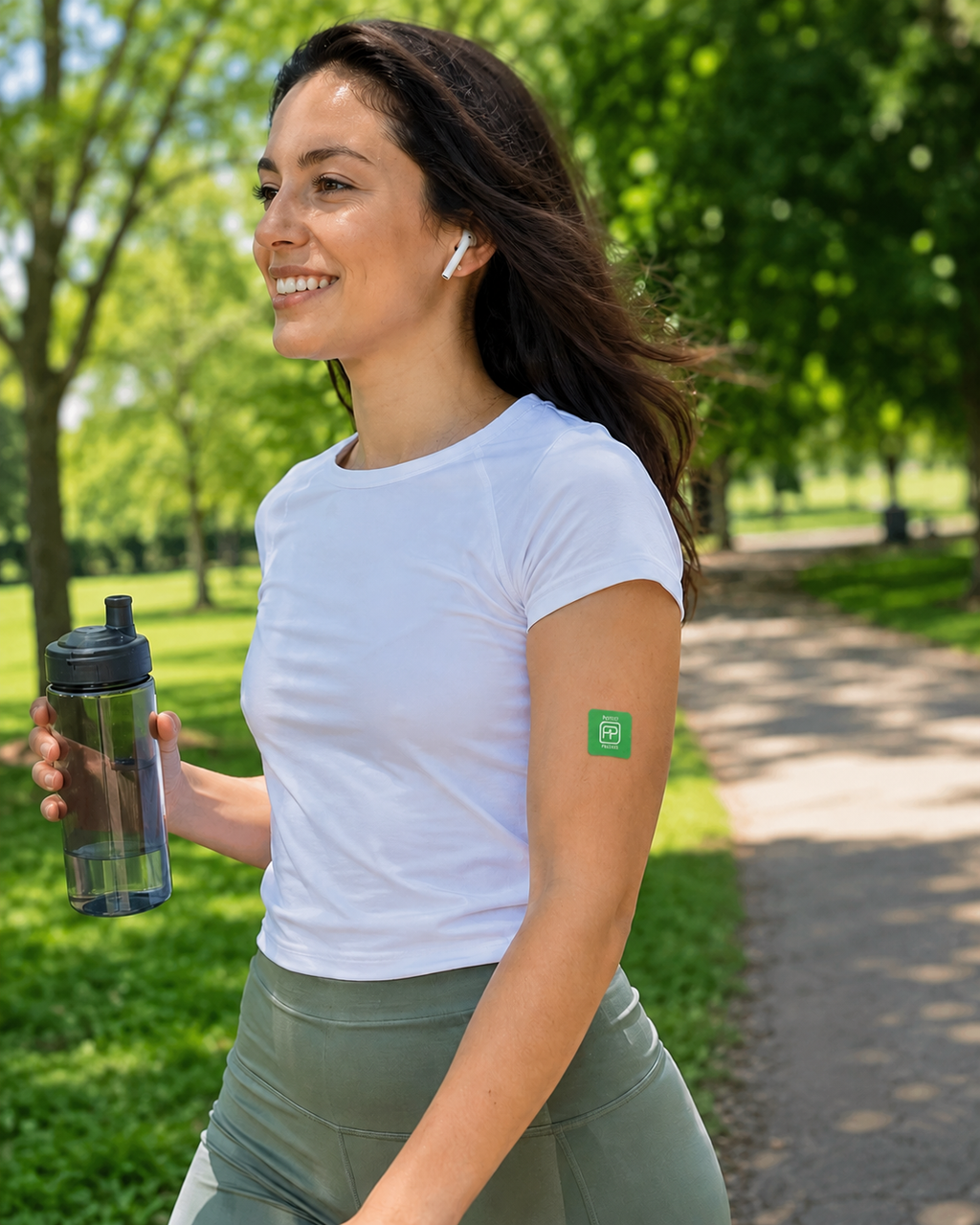 Woman walking in a park with earbuds and a water bottle, wearing a green Feel Good patch on her upper arm