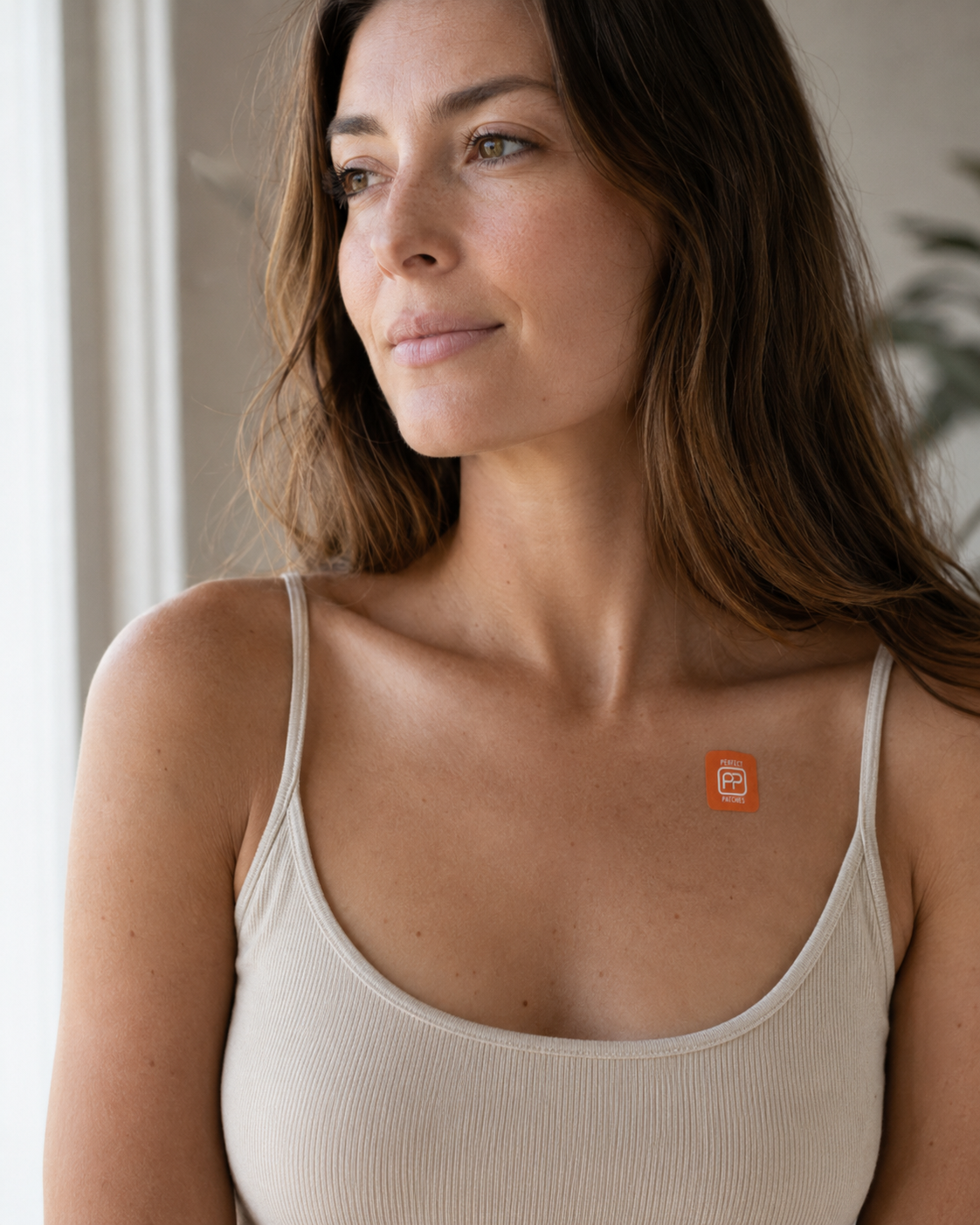 Woman looking out of a window wearing an orange Mood patch on her collarbone