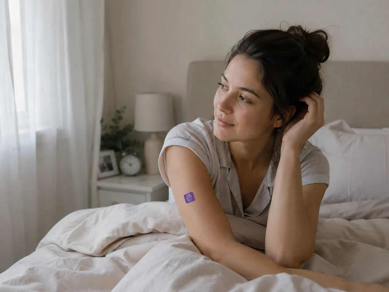 Someone resting on a bed in a bright bedroom, wearing a purple Bedtime patch on their upper arm